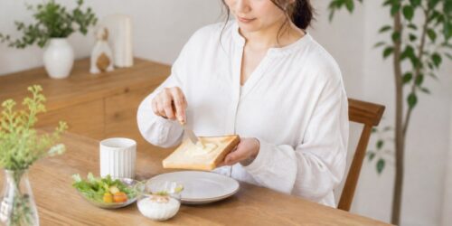 食卓でトーストにはちみつを塗っている女性